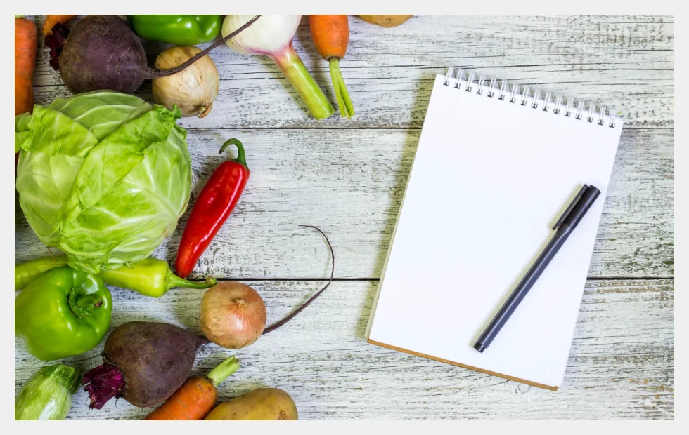 Fresh vegetables and notebook on table